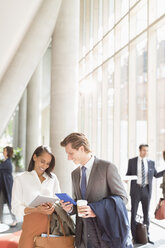 Business people using digital tablets talking in sunny office lobby - CAIF06257