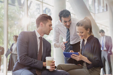 Business people with coffee using digital tablet, talking in office lobby - CAIF06273