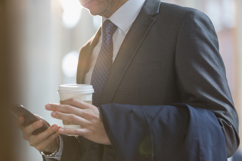 Nahaufnahme Geschäftsmann im Anzug mit Kaffee, der mit seinem Handy SMS schreibt, lizenzfreies Stockfoto