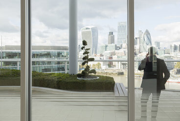 Geschäftsmann, der auf einem Balkon mit Blick auf die Stadt London mit einem Handy telefoniert, London, Großbritannien - CAIF06282