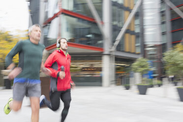 Männer mit Kopfhörern, die auf einem städtischen Bürgersteig laufen - CAIF06304