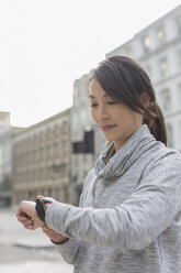 Female runner checking smart watch on urban street - CAIF06313