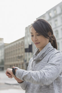 Läuferin überprüft Smartwatch auf städtischer Straße - CAIF06313