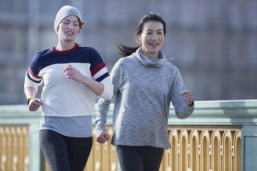 Smiling female runners running along railing - CAIF06331