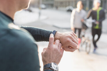 Male runner checking smart watch on urban sidewalk - CAIF06338