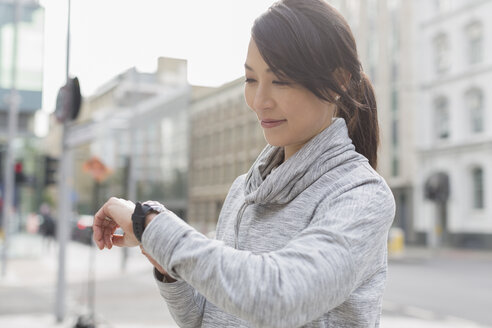 Lächelnde Läuferin, die auf einem städtischen Bürgersteig ihre Armbanduhr überprüft - CAIF06341