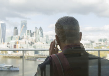 Geschäftsmann, der auf einem städtischen Balkon mit Blick auf die Stadt mit einem Handy telefoniert, London, UK - CAIF06347