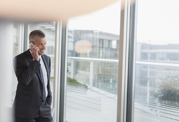 Geschäftsmann, der am Bürofenster mit seinem Handy telefoniert - CAIF06353