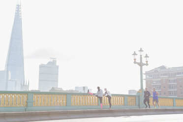 Läufer beim Laufen und Dehnen auf einer sonnigen, nebligen Stadtbrücke, London, UK - CAIF06355