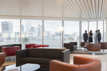 Geschäftsleute im Gespräch am Fenster in einer städtischen Hochhaus-Büro-Lounge mit Blick auf die Stadt - CAIF06359