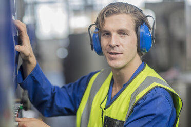 Portrait of man wearing ear defenders operating machine in factory - ZEF15142