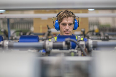 Mann mit Gehörschutz bei der Bedienung einer Maschine in einer Fabrik - ZEF15155