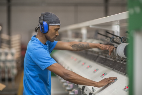 Mann mit Gehörschutz bei der Bedienung einer Maschine in einer Fabrik, lizenzfreies Stockfoto