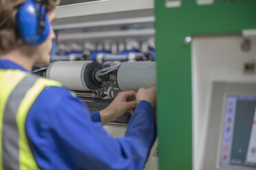 Mann mit Gehörschutz bei der Arbeit an einer Spulenmaschine in einer Fabrik - ZEF15158