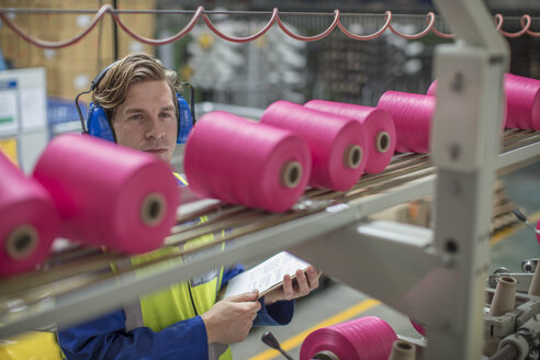 Man wearing ear defenders working at spool machine in factory - ZEF15160
