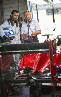 Manager und Formel-1-Rennfahrer unterhalten sich in der Reparaturwerkstatt - CAIF06397