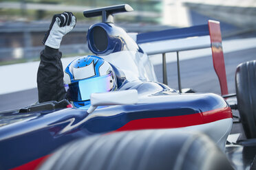 Porträt eines Formel-1-Rennfahrers, der einen Helm trägt und mit der Faust jubelt, auf einer Sportstrecke - CAIF06402