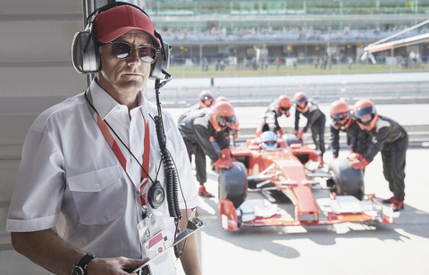 Porträt eines seriösen Managers mit einem Formel-1-Rennwagen und einer Boxenmannschaft im Hintergrund, lizenzfreies Stockfoto