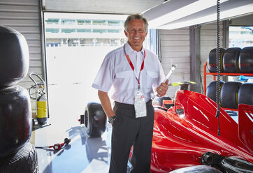 Portrait confident formula one manager next to race car in repair garage - CAIF06426