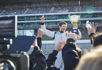 Ein Formel-1-Rennteam bespritzt einen Fahrer mit einer Trophäe mit Champagner und feiert den Sieg auf einer Sportstrecke - CAIF06430