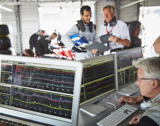 Formula one racing team reviewing diagnostics on computers in repair garage - CAIF06437