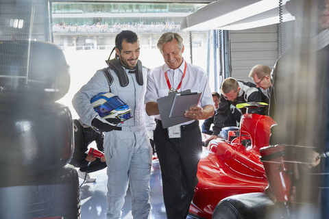 Manager und Formel-1-Rennfahrer unterhalten sich in der Reparaturwerkstatt, lizenzfreies Stockfoto