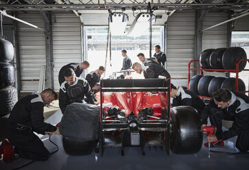 Pit crew working on formula one race car in repair garage - CAIF06453