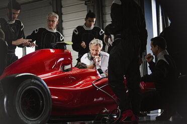 Manager und Boxencrew bei der Arbeit an einem Formel-1-Rennwagen in einer dunklen Reparaturwerkstatt - CAIF06471
