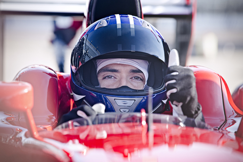 Porträt eines selbstbewussten männlichen Formel-Eins-Rennfahrers, der den Daumen nach oben streckt, lizenzfreies Stockfoto