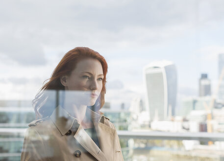 Selbstbewusste Geschäftsfrau mit roten Haaren auf städtischem Balkon mit Blick auf die Stadt - CAIF06546