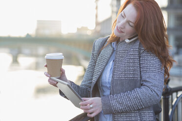 Geschäftsfrau beim Multitasking, Kaffeetrinken und Benutzen des digitalen Tisches, während sie mit dem Handy telefoniert - CAIF06551