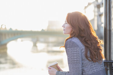 Serene businesswoman with red hair drinking coffee at urban waterfront - CAIF06556