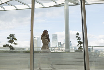 Businesswoman talking on cell phone on urban balcony with city view - CAIF06562