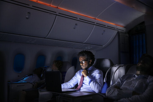 Businessman working at laptop on night airplane - CAIF06566