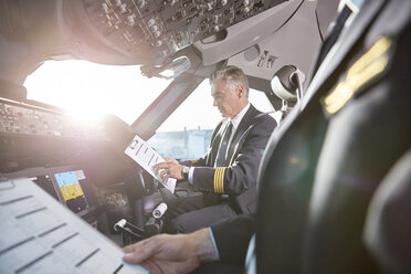 Männliche Piloten mit Klemmbrett, die sich im Cockpit eines Flugzeugs vorbereiten - CAIF06573