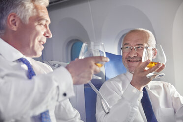 Geschäftsmann stößt in der ersten Klasse eines Flugzeugs mit Whiskeygläsern an - CAIF06577