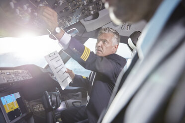 Männlicher Pilot mit Klemmbrett, der im Cockpit eines Flugzeugs Instrumente einstellt - CAIF06578