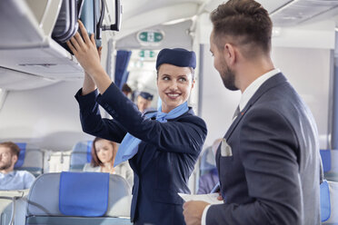 Flugbegleiter hilft Geschäftsmann mit Gepäck im Flugzeug - CAIF06581