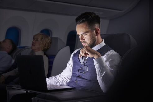 Seriöser Geschäftsmann arbeitet im Flugzeug über Nacht am Laptop - CAIF06592