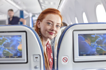 Portrait lächelnde junge Frau mit roten Haaren und Sommersprossen im Flugzeug - CAIF06595