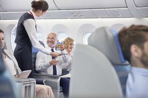 Flugbegleiter serviert Geschäftsmann in der ersten Klasse Whiskey im Flugzeug, lizenzfreies Stockfoto