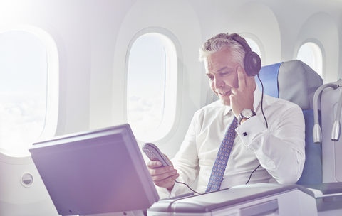 Geschäftsmann mit Kopfhörern schaut Film im Flugzeug, lizenzfreies Stockfoto