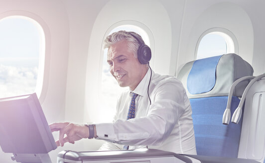 Geschäftsmann mit Kopfhörern schaut Film im Flugzeug - CAIF06601