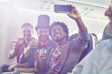 Enthusiastische junge männliche Freunde mit Fotohandy trinken und nehmen Selfie im Flugzeug - CAIF06604