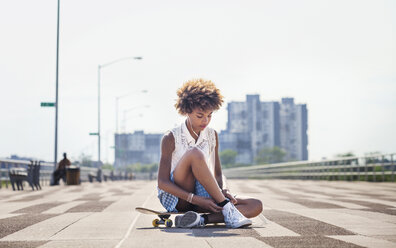 Teenager hört Musik, während er auf dem Skateboard sitzt - CAVF01104