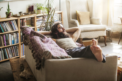 Thoughtful man relaxing on sofa at home - CAVF01144
