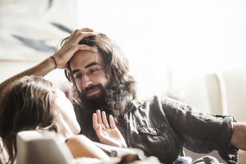 Mann schaut Frau an, während er zu Hause auf dem Sofa sitzt, lizenzfreies Stockfoto