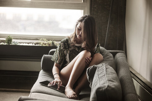 Woman using tablet computer while sitting on sofa - CAVF01176