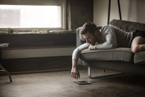 Mann schaut auf Tablet-Computer, während er auf dem Sofa liegt - CAVF01182