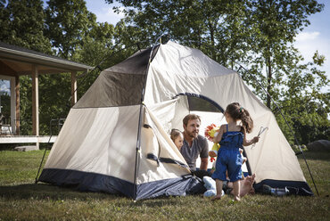 Vater mit Kindern schaut Mädchen an, während er im Zelt sitzt - CAVF01196